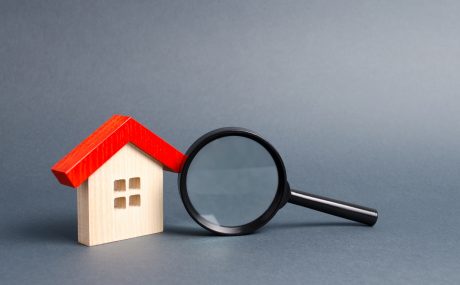 Wooden house and magnifying glass on a gray background